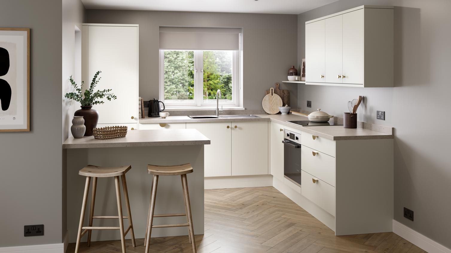 A warm white kitchen with slab doors in a peninsula layout. There are stone-effect worktops and herringbone oak flooring.