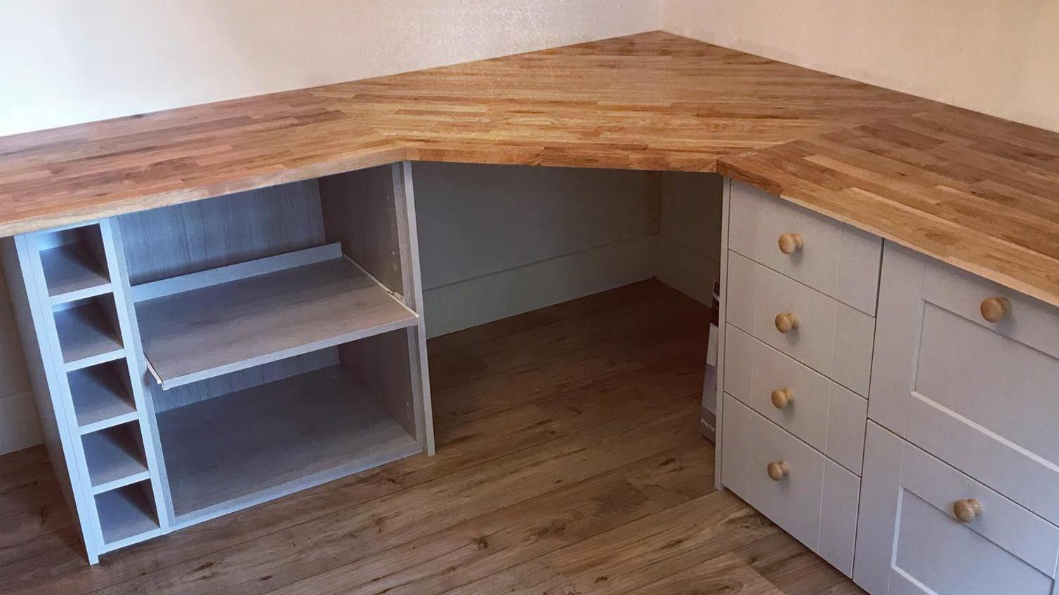 Home office idea with a dark oak desk, light grey shaker drawers and cupboards, and matching dark wood flooring.