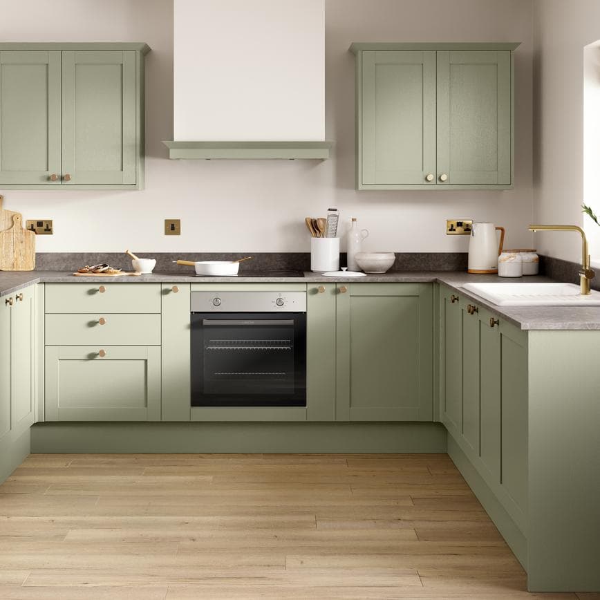 An l-shaped shaker kitchen in a pale, reed green colour. It has grey stone worktops and oak-style, laminate plank flooring.