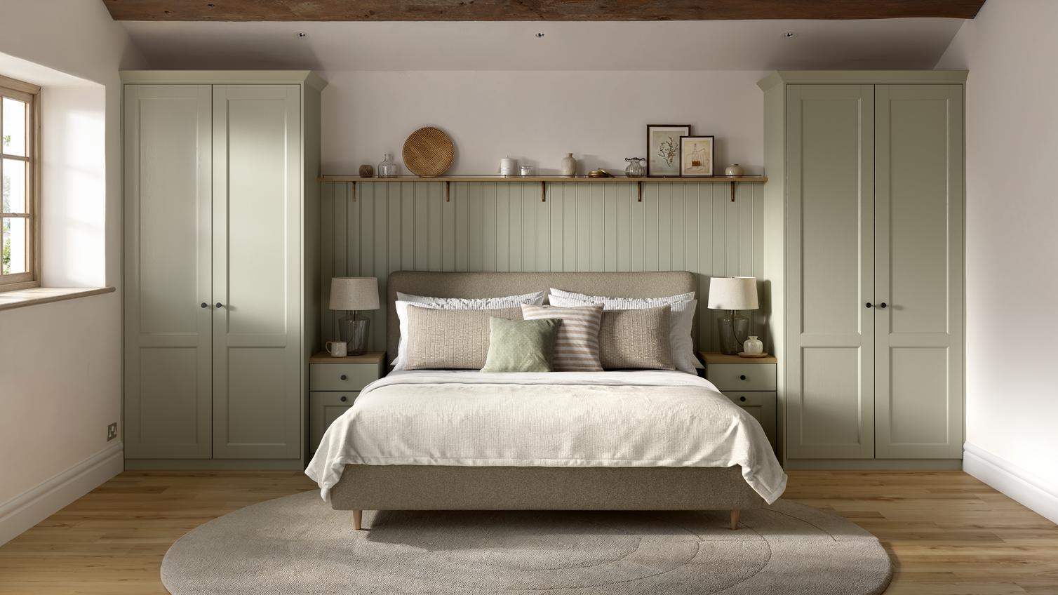 A Bridgemere bedroom with shaker wardrobes in a sage green tone. There is matching, painted wall panels & shelves above.